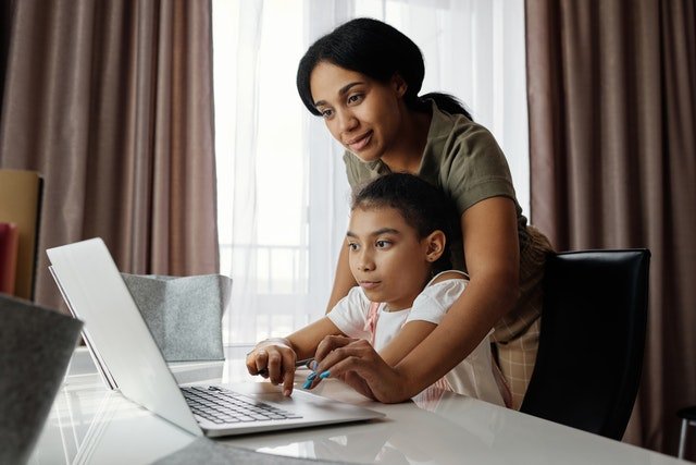 mom guiding daughter to use laptop