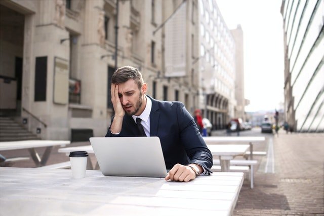 man holding head while using laptop